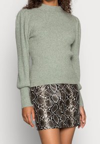 Pull côtelé vert clair avec manches bouffantes, assorti à une mini-jupe ajustée à imprimé serpent noir et blanc. Les deux vêtements ont des textures lisses.