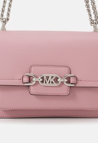 Růžová kožená taška přes rameno s kovovým řetízkovým uchopem a charakteristickým kovovým logem MK na předním klopě. Hladká textura a štíhlý design.