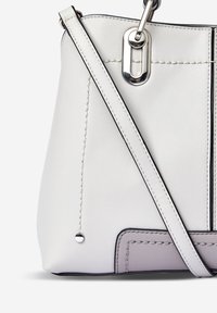 Biała skórzana torebka z kontrastującymi szwami, srebrnymi akcentami oraz jedną regulowaną rączką. Posiada teksturowane dno i dekoracyjny metalowy detal.
