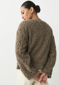 Brązowy, teksturowany sweter z polaru o luźnym kroju, z prążkowanym dołem i szerokimi rękawami. Wyraźny wzór 3D nadaje tkaninie głębię i interesujący wygląd.