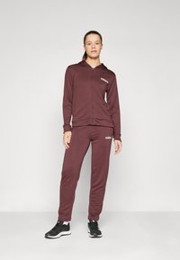 Maroon zip-up hoodie and matching joggers made of soft fabric, featuring the adidas logo in white on the chest and thigh. Black athletic shoes.