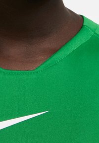 Vihreä urheilupaita V-kaula-aukkolla, valmistettu sileästä kankaasta, jossa vasemmalla rinnalla valkoinen Nike-swoosh-logo.