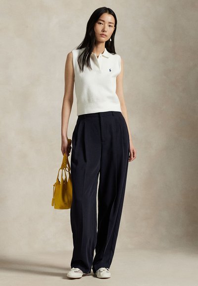 Sleeveless white polo top with ribbed texture, paired with high-waisted navy pants. Holding a structured yellow handbag, wearing white shoes.