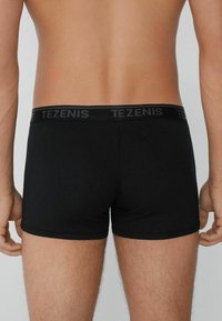 Boxers negros ajustados en una tela suave y elástica. Presentan una cinturilla elástica con "TEZENIS" en letras oscuras. Diseño simple y ajustado.