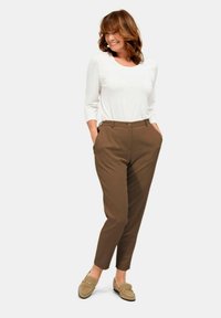 Brown tailored trousers with a smooth fabric, a classic fit, and two side pockets. Paired with a white long-sleeve top and beige loafers.