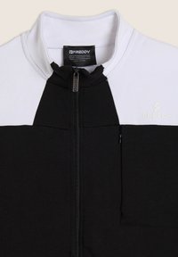 Sudadera con cremallera en blanco y negro, con cuello alto, bolsillo en el pecho izquierdo, tela texturizada y logotipo "FREDDY" en el frente.