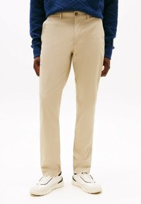 Beige chinos laget av vevd stoff, rett kutt, med frontknapp-lukking og sidelommer, kombinert med hvite sneakers.
