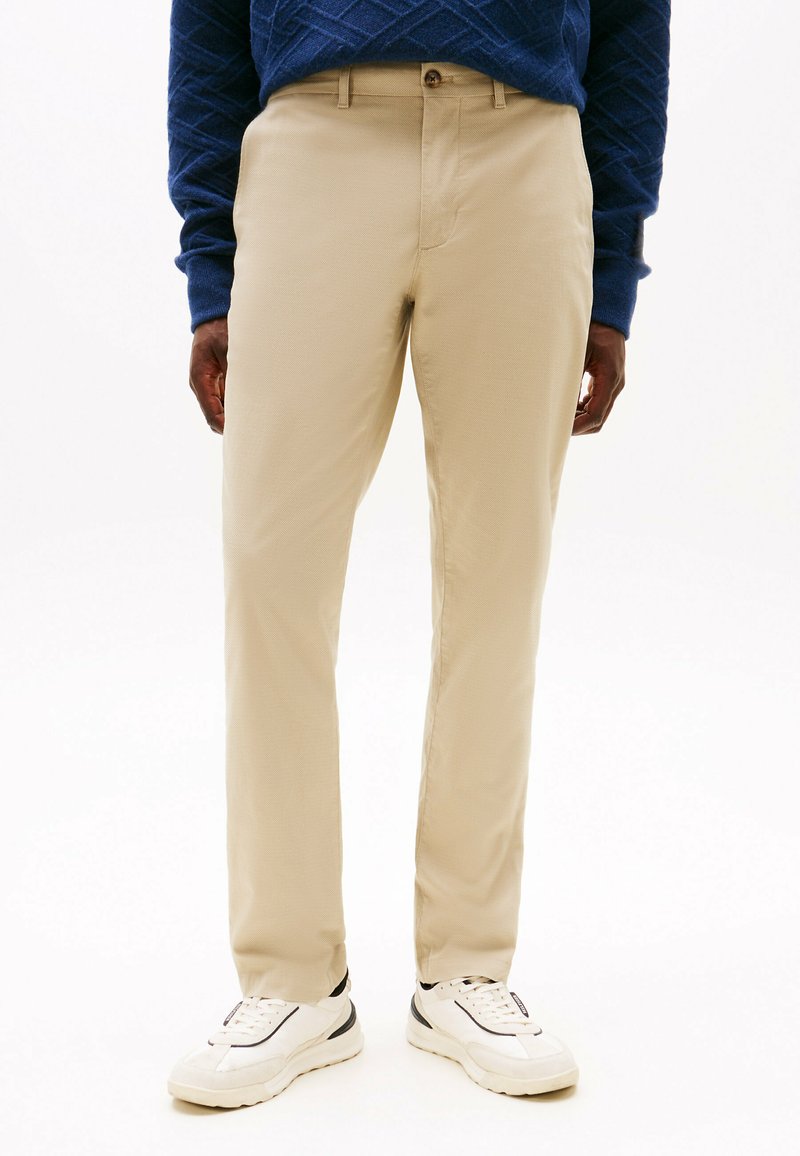 Beige chinos laget av vevd stoff, rett kutt, med frontknapp-lukking og sidelommer, kombinert med hvite sneakers.