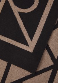 Tissu noir et beige à motif présentant des formes géométriques, avec une surface texturée et des accents de couleur contrastés dans des designs audacieux.