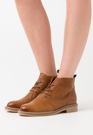 Bottes chelsea en cuir marron avec une finition texturée, dotées de lacets, d'un bout arrondi et d'une semelle de couleur claire, adaptées à un usage décontracté.