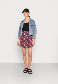 Chaqueta de mezclilla, top corto de canalé negro, falda mini floral en rojo y azul, y sandalias negras. Presenta un atuendo casual en capas.