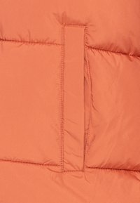 Närbild av en vertikal ficka med slits på orange vadderad tyg med synliga sömmar och mjuk textur.