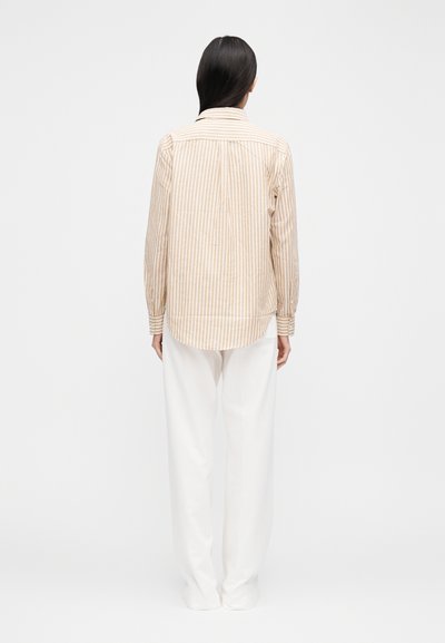 Pruhovaná košeľa s dlhým rukávom v béžovej a bielej farbe, s chrbtovým dielom a zaobleným lemom. Kombinovaná s voľnými bielymi nohavicami.