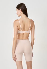 Soutien-gorge beige con spalline regolabili e chiusura a gancio, abbinato a pantaloni modellanti lunga ginocchio, entrambi realizzati in tessuto morbido ed elastico.