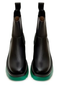 Botas de cuero negro hasta el tobillo con un acabado liso, que presentan una puntera redondeada y una suela de goma verde. Incluyen tiradores para facilitar el calzado y descalzado.