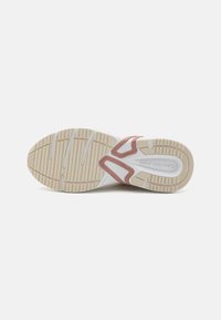 Fehér sneaker bézs gumitalppal, mintázott talppal. Részletei között szerepel egy rózsaszín kiegészítő az oldalon, és sima, texturált felsőrész.
