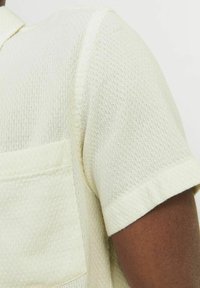 Chemise à manches courtes de couleur jaune clair, avec un motif en nid d'abeille texturé, une poche poitrine et un col pointu.