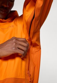 Henkilö, jolla on oranssi takki, avaa ilmanvaihtovetoketjua nostetun käden alta.