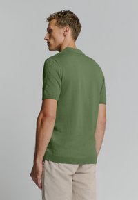 Groene polo shirt met korte mouwen en een gestructureerd ruitpatroon op de schouders, voorzien van een klassieke kraag. Soepele stof, ontspannen pasvorm.