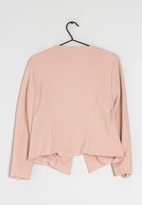 Roze lange mouwen jas met een gestructureerd ontwerp, geribbelde textuur, een verlengd achterpand en een ronde halslijn. Hangt aan een zwarte haak.