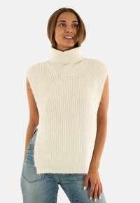 Maglione bianco smanicato a collo alto, con texture a costine e vestibilità ampia, abbinato a jeans in denim.