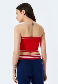 Top corto rojo sin tirantes con un diseño ajustado y rayas blancas contrastantes a lo largo del dobladillo. Se lleva con pantalones azul marino.
