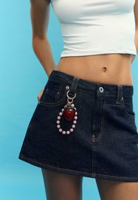 Denim mini suknja s zlatnim detaljima, koja sadrži privjesak u obliku jagode i ključanicu s ružičastim perlicama koja visi s petlje za remen.