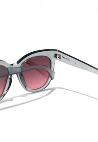 Ochelari de soare cu lentile în formă de ochi de pisică, cu rame transparente gri și lentile roz degrade. Finisaj mat cu accesorii argintii pe brațele ochelarilor.