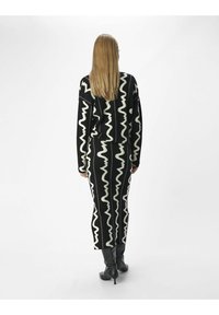 Ensemble tricoté avec un motif zigzag noir et crème, comprenant un pull à coupe décontractée et une jupe longue. Porté avec des bottes noires à talons aiguilles montantes.