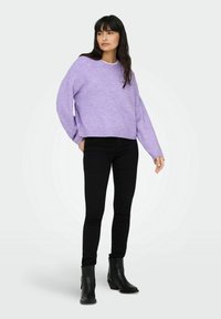 Pull en tricot lilas avec un col rond et des épaules tombantes, associé à un jean noir slim et des bottines noires. Design simple, texture douce.
