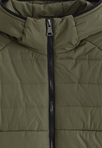 Veste matelassée vert olive avec une fermeture éclair noire et un col montant, présentant des détails de surpiqûres horizontales matelassées.