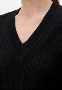 Schwarzer, leichter Strickpullover mit V-Ausschnitt, der offene Netzdetails auf den Schultern und eine gleichmäßige, glatte Textur aufweist.
