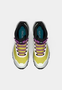 Zapatos de senderismo ligeros con un upper en amarillo y gris, cuello negro y cordones morados. Diseñados con una suela de goma para proporcionar tracción.