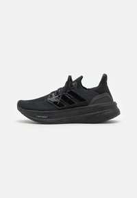 Baskets de course Adidas Ultraboost noires avec tige en tricot, fermeture à lacets et semelle épaisse et rembourrée sur fond blanc.