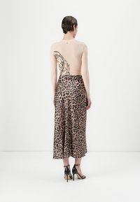 Top a maniche lunghe nudo con una grafica nera sul retro, abbinato a una gonna a lunghezza midi con stampa leopardata e sandali neri con tacco alto.