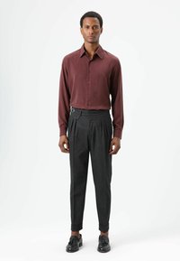 Bordeauxrood shirt met lange mouwen gecombineerd met grijze geplooide broek met een decoratieve riemgesp en omgeslagen broekzomen. Zwarte schoenen maken de outfit compleet.