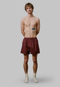 Boxers rouges et noirs à rayures avec une ceinture élastique, fabriqués en tissu léger, portés avec des chaussettes blanches, présentés sur un fond gris.
