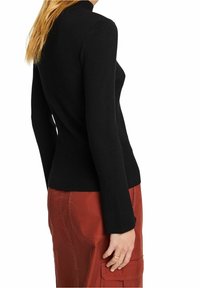 Schwarzes, geripptes Langarmoberteil mit figurbetontem Schnitt und hohem Kragen, kombiniert mit einem roten Rock aus strukturiertem Stoff.