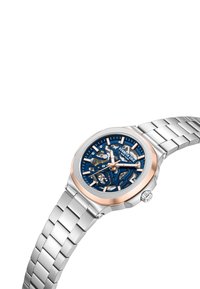Silverfärgad klocka i rostfritt stål med en blå mönstrad skelettskiva. Har roséguldiga detaljer på ramen och visarna, samt ett länkarmband.