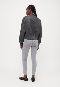 Grå skinn bomberjakke med ribbede mansjetter og hem, kombinert med slanke grå jeans og svarte ballettsko, sett fra bak.