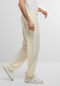 Pantalones de color crema claro, con un corte relajado, hechos de una tela suave, que cuentan con una cinturilla elástica y bolsillos laterales. Combinados con zapatillas blancas.
