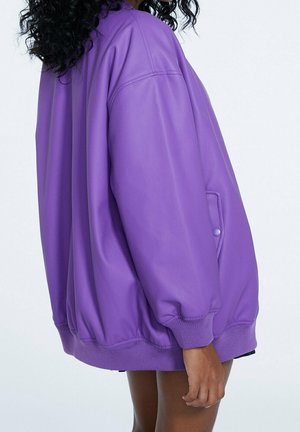 Purple faux leather bomber jacket with oversized fit, ribbed cuffs, and a pocket featuring a round button detail. Smooth texture.