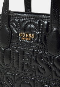 Sort håndtaske med quiltet tekstur, har prægede branding og detaljer i guld hardware, struktureret form og dobbelthåndtag.