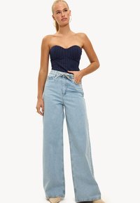 Marineblauw strapless top met een pinstripe ontwerp, gecombineerd met lichtblauwe wijdbenige jeans met hoge taille en klassieke denimplooien.