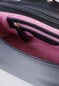 Svart läderhandväska med texturerad yta. Insidan har rosa tygfodring med ett upprepat mönster av varumärket och en svart dragkedjeficka.