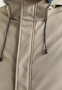 Béžová bunda s kapucí a středovým zipem zakrytým légou, černé šňůrky s plastovými tipy na kapuci.