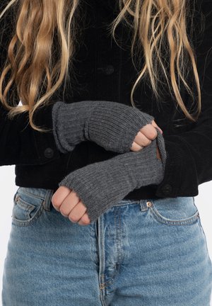 Grijze gebreide vingerloze handschoenen met ribbeltextuur, gedragen met een zwarte corduroy jas. De handschoenen reiken tot de pols en hebben een strak pasvorm.