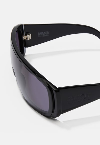 Óculos de sol pretos com um design elegante, lentes degradé e logótipos distintos nas hastes. As armações são suaves e ligeiramente curvadas.