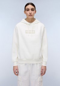 Witte hoodie gemaakt van zacht stof, met een logo patch aan de voorkant, ribgebreide manchetten en zoom, gecombineerd met lichtgekleurde cargobroek.