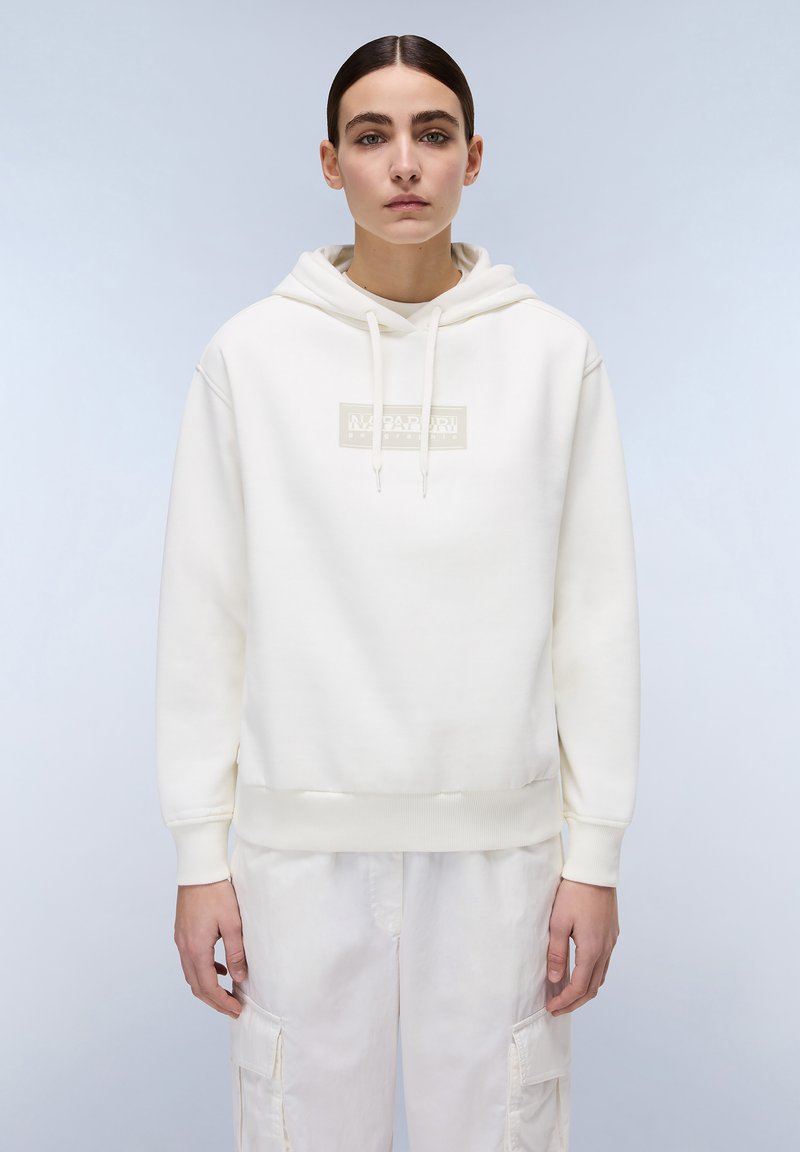 Witte hoodie gemaakt van zacht stof, met een logo patch aan de voorkant, ribgebreide manchetten en zoom, gecombineerd met lichtgekleurde cargobroek.